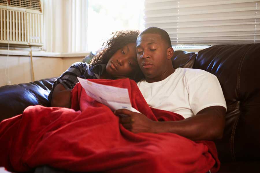young couple on couch looking unhappy whilst looking at energy bill