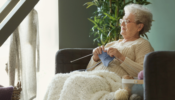 older lady with layers knitting on couch keeping warm